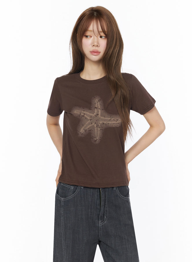 Star Graphic Tee IU525 Brown front model shot with faded star graphic print on fitted cotton tee styled with dark wide-leg jeans hands behind back