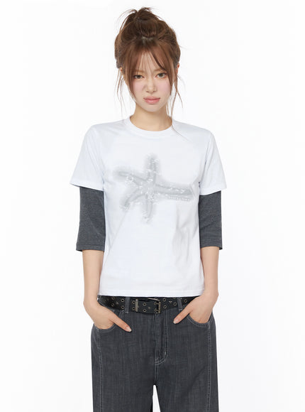 Star Graphic Tee IU525 White front model shot with star graphic layered over gray long-sleeve tee hands in pockets styled with dark wide-leg denim and eyelet belt