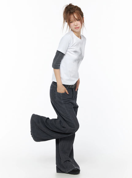 Star Graphic Tee IU525 White side model shot with one leg raised showing relaxed fit layered over gray long-sleeve tee styled with wide-leg dark denim