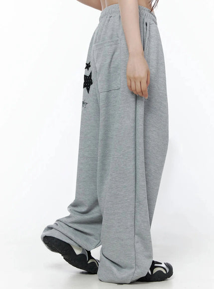 Star Graphic Wide Leg Sweatpants IL506 Gray side close-up on model walking showing black polka-dot and plaid star appliqués on thigh