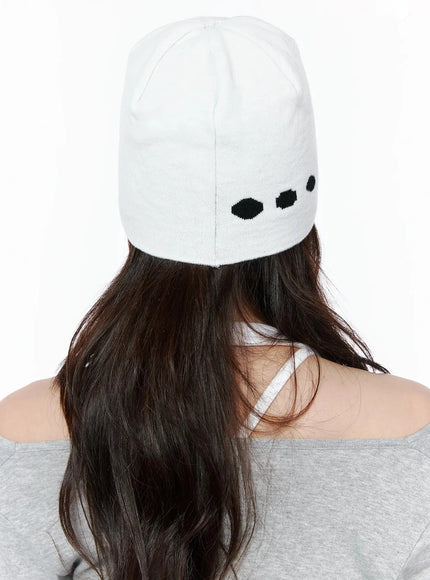 Star Knit Beanie IL506 White back on-model close-up, female model facing away, white knit beanie with minimal black dot pattern visible at crown, raw overlock top seam detail