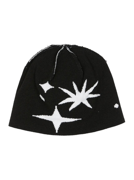 Star Knit Beanie IL506 Black flat product shot, black knit beanie laid flat showing white starburst and four-point star intarsia pattern with exposed overlock seam at crown