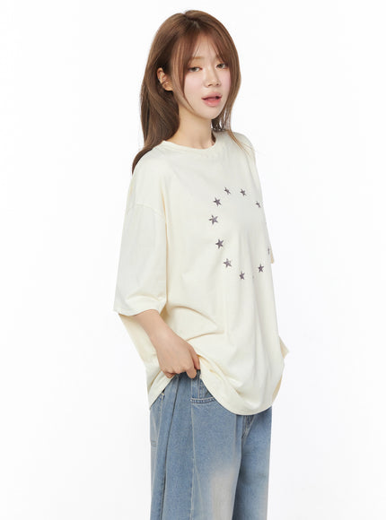Star Ring Graphic Oversized Tee IL502 Light beige angled front shot model hand in pocket showing circular star graphic dropped sleeves and oversized silhouette