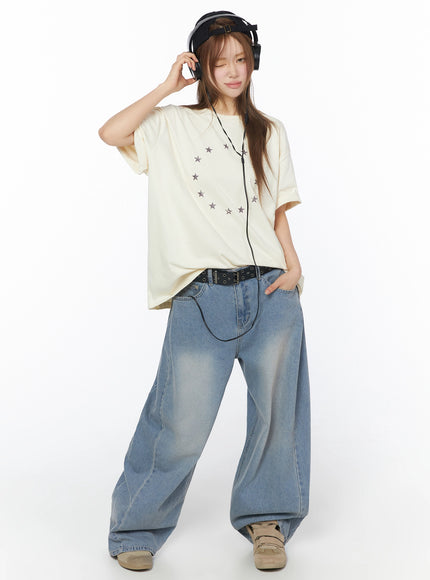 Star Ring Graphic Oversized Tee IL502 Light beige full-body front shot model wearing headphones cap and belt styled with wide-leg jeans and chunky sneakers