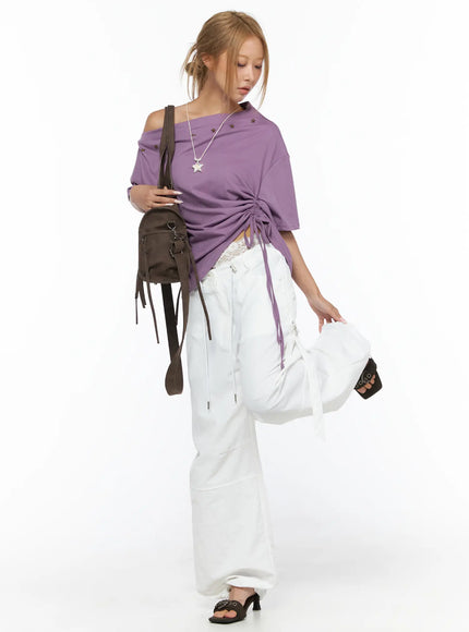 Star Studded Asymmetric Drawstring Tee CU524 Purple full-body lifestyle shot on model with brown shoulder bag and star necklace, leg raised, styled with white trousers and black heeled mules