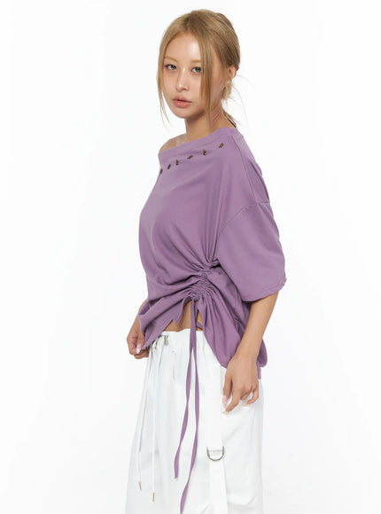 Star Studded Asymmetric Drawstring Tee CU524 Purple angled front shot on model showing bronze star stud neckline detail, side ruching with drawstring, paired with white cargo pants