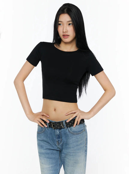 Stretch Crop Tee IL509 Black front half-body shot on model hands on hips gazing upward showing fitted crop silhouette with blue jeans and eyelet belt