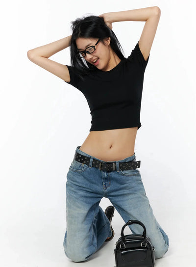 LEWKIN Stretch Crop Tee IL509 Black S/M dynamic kneeling pose on model wearing glasses with arms raised styled with blue jeans and black bag
