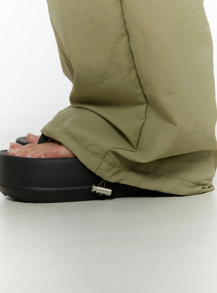 String Pocket Wide Pants CU526 Dark green close-up detail of gathered hem pooling over black platform sandals showing lightweight nylon texture and hem cinch