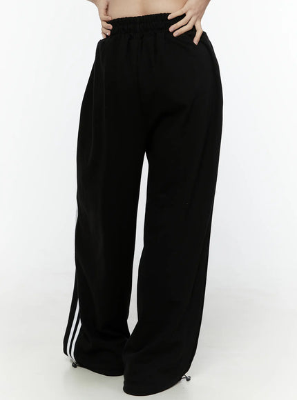 Stripe Detail Sweatpants IL506 Black back waist close-up on model, hands on elastic waistband, wide-leg fit with white side stripes partially visible