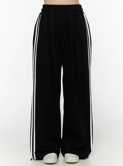 LEWKIN Stripe Detail Sweatpants IL506 Black front view on model, headless shot, wide-leg silhouette with white side stripes, elastic drawstring waist, S/M
