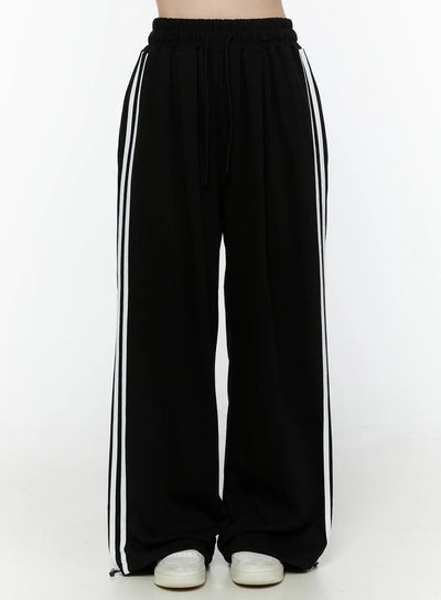 LEWKIN Stripe Detail Sweatpants IL506 Black front view on model, headless shot, wide-leg silhouette with white side stripes, elastic drawstring waist, S/M
