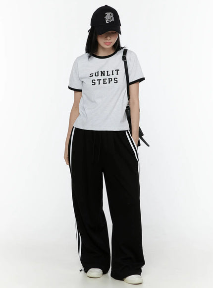 Stripe Detail Sweatpants IL506 Black full-body model shot, styled with grey tee, black cap, and crossbody bag, wide-leg silhouette with white side stripes