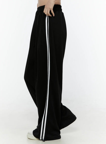 Stripe Detail Sweatpants IL506 Black side view on model, hand at waistband, wide-leg silhouette with white contrast stripe running full length of leg