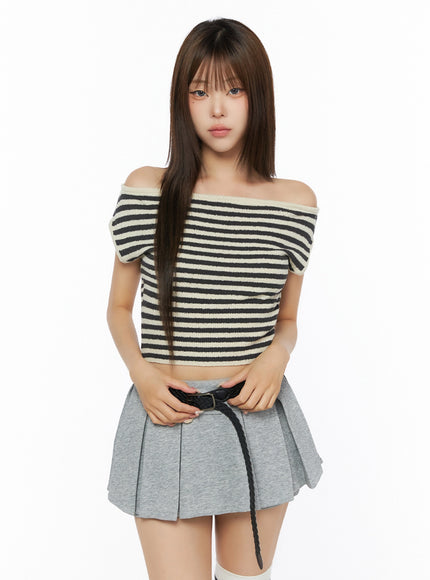 Stripe Off-Shoulder Knit Top IL506 Ivory front view on model standing straight, off-shoulder neckline with black horizontal stripes, paired with gray pleated mini skirt