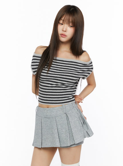 Stripe Off-Shoulder Knit Top IL506 Gray front view on model with downward gaze, hand on hip, cropped off-shoulder knit top styled with gray pleated mini skirt without belt