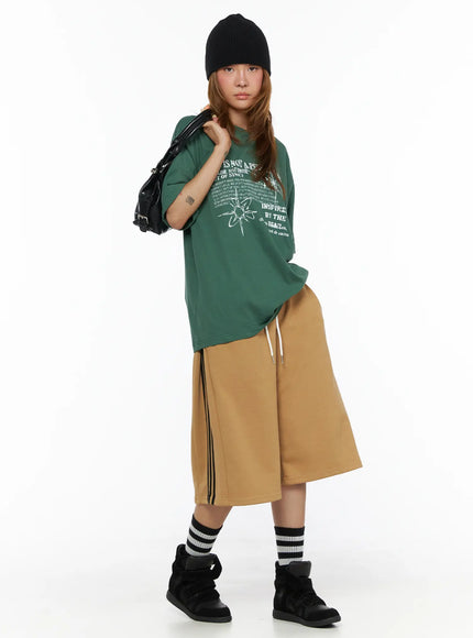 LEWKIN Striped Bermuda Shorts CL503 Beige S/M full-body front on model wearing black beanie, styled with green graphic tee, striped socks and black sneakers