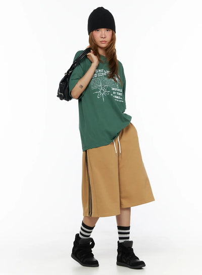 LEWKIN Striped Bermuda Shorts CL503 Beige S/M full-body front on model wearing black beanie, styled with green graphic tee, striped socks and black sneakers