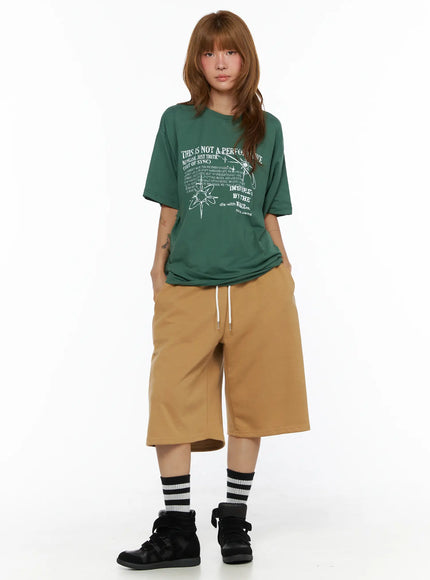 Striped Bermuda Shorts CL503 Beige front full-body on model standing straight, styled with green graphic oversized tee, hands in pockets, striped socks and black sneakers