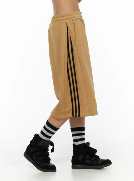 Striped Bermuda Shorts CL503 Beige side close-up on model highlighting triple black side stripe, pleated panel, elastic waistband and wide-leg fleece fabric texture
