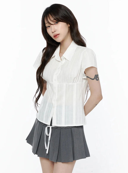 Striped Button-Up Blouse IL506 White three-quarter side front shot on model with hand in pocket showing empire waist seam and sheer stripe fabric with gray pleated skirt