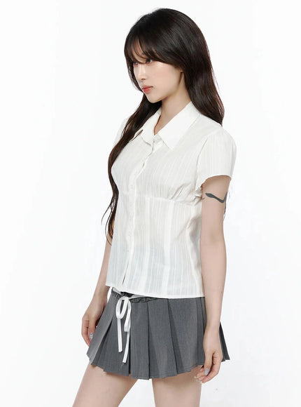 Striped Button-Up Blouse IL506 White three-quarter side shot on model showing fitted silhouette, point collar, short sleeves, and vertical stripe texture with gray pleated skirt
