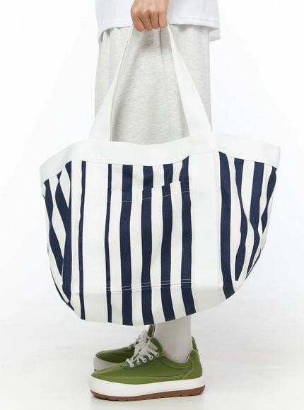 Striped Canvas Tote Bag IL514 Dark blue front shot on model holding bag by handles at waist level, navy stripe oversized canvas tote with cap inside, green sneakers