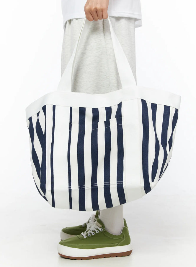 Striped Canvas Tote Bag IL514 Dark blue front shot on model holding bag by handles at waist level, navy stripe oversized canvas tote with cap inside, green sneakers