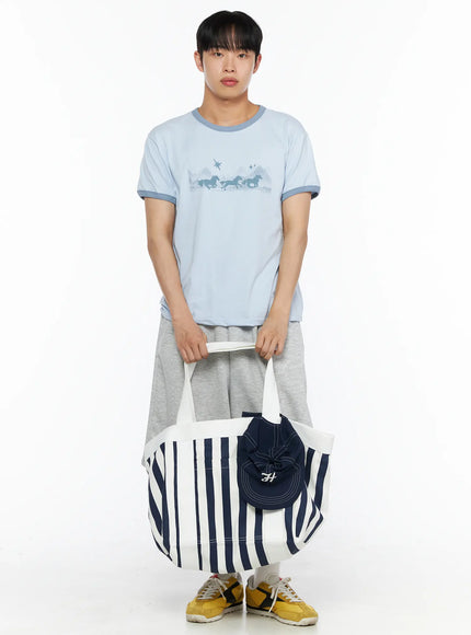 Striped Canvas Tote Bag IL514 Dark blue side shot on male model carrying navy stripe canvas tote on shoulder, styled with light blue graphic tee and grey shorts