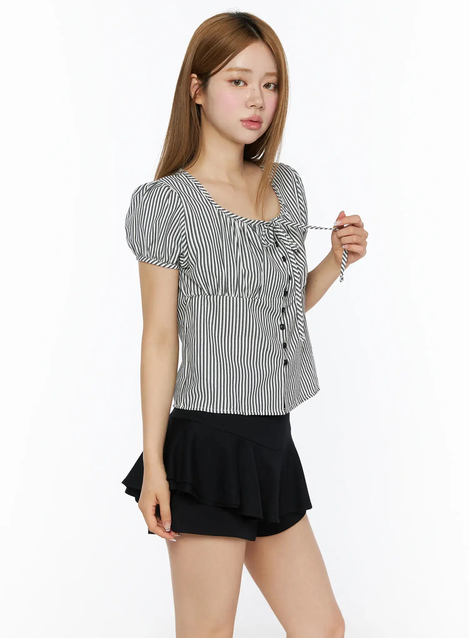 Striped Puff Short Sleeve Blouse CL502 Black three-quarter side shot on model holding tie cord detail at neckline, puff sleeves, button-front, paired with black mini skirt