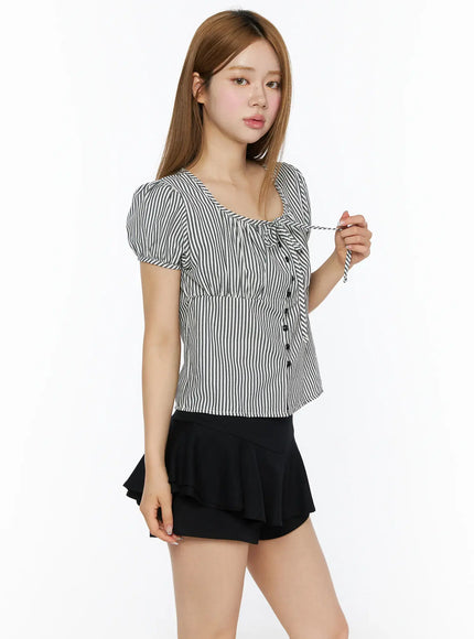 Striped Puff Short Sleeve Blouse CL502 Black three-quarter side shot on model holding tie cord detail at neckline, puff sleeves, button-front, paired with black mini skirt