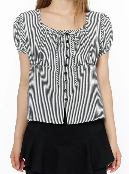 Striped Puff Short Sleeve Blouse CL502 Black close-up front detail shot on model showing scoop neckline, tie detail, black button-front closure, ruched chest, and cinched elastic waist
