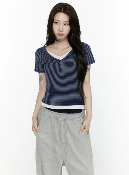 Striped T-Shirt IL522 Navy front shot on model with hands in pockets, fitted short-sleeve navy horizontal stripe henley tee with cream contrast V-neck and ribbed hem, styled with gray sweatpants
