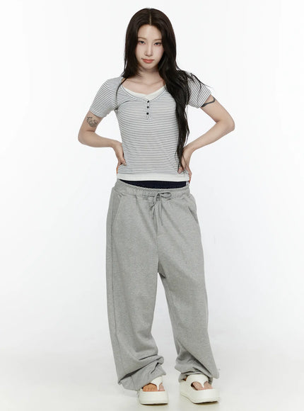 Striped T-Shirt IL522 White full-body front shot on model hands on hips, slim-fit short-sleeve striped henley tee with cream ribbed hem, paired with gray jogger pants and white sandals