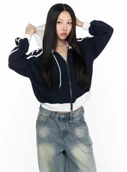 Striped Track Hoodie CL524 Dark blue front shot on model pulling up white hood with both hands, zip partially open showing inner layer, white stripe sleeves, cropped fit