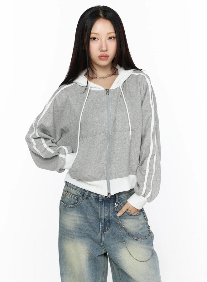 Striped Track Hoodie CL524 gray front shot on model standing, zip-up cropped hoodie with white double stripes on sleeves and ribbed hem, styled with faded jeans