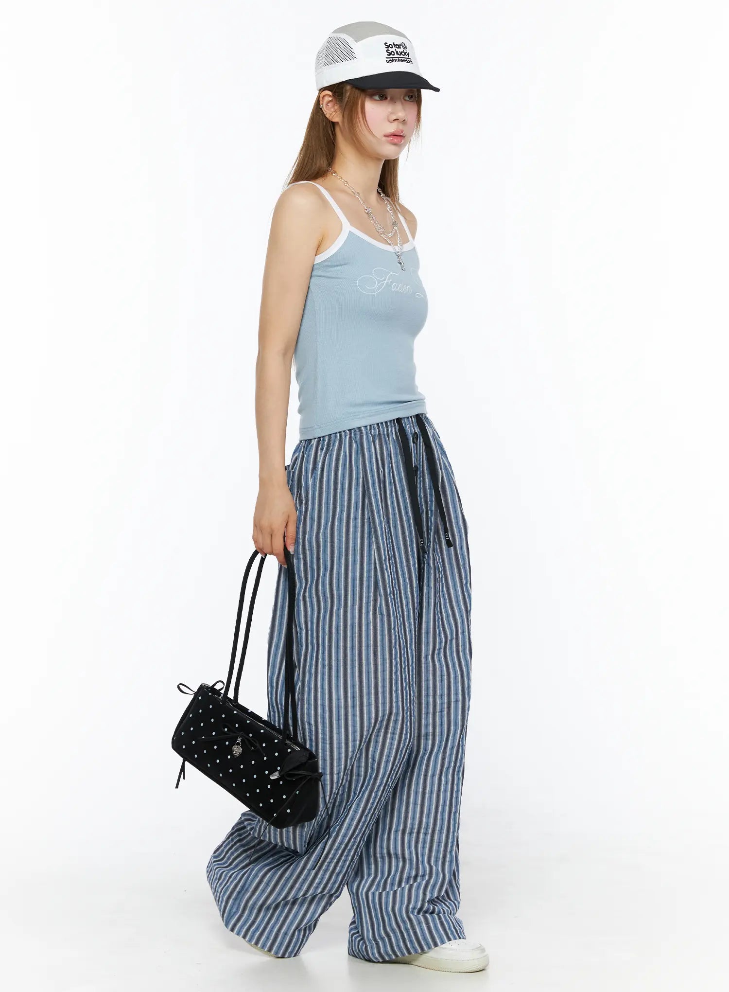 LEWKIN Striped Wide-Leg Trousers CL502 Blue M/L side shot on model wearing trucker cap and carrying black studded bag with wide crinkle stripe pants