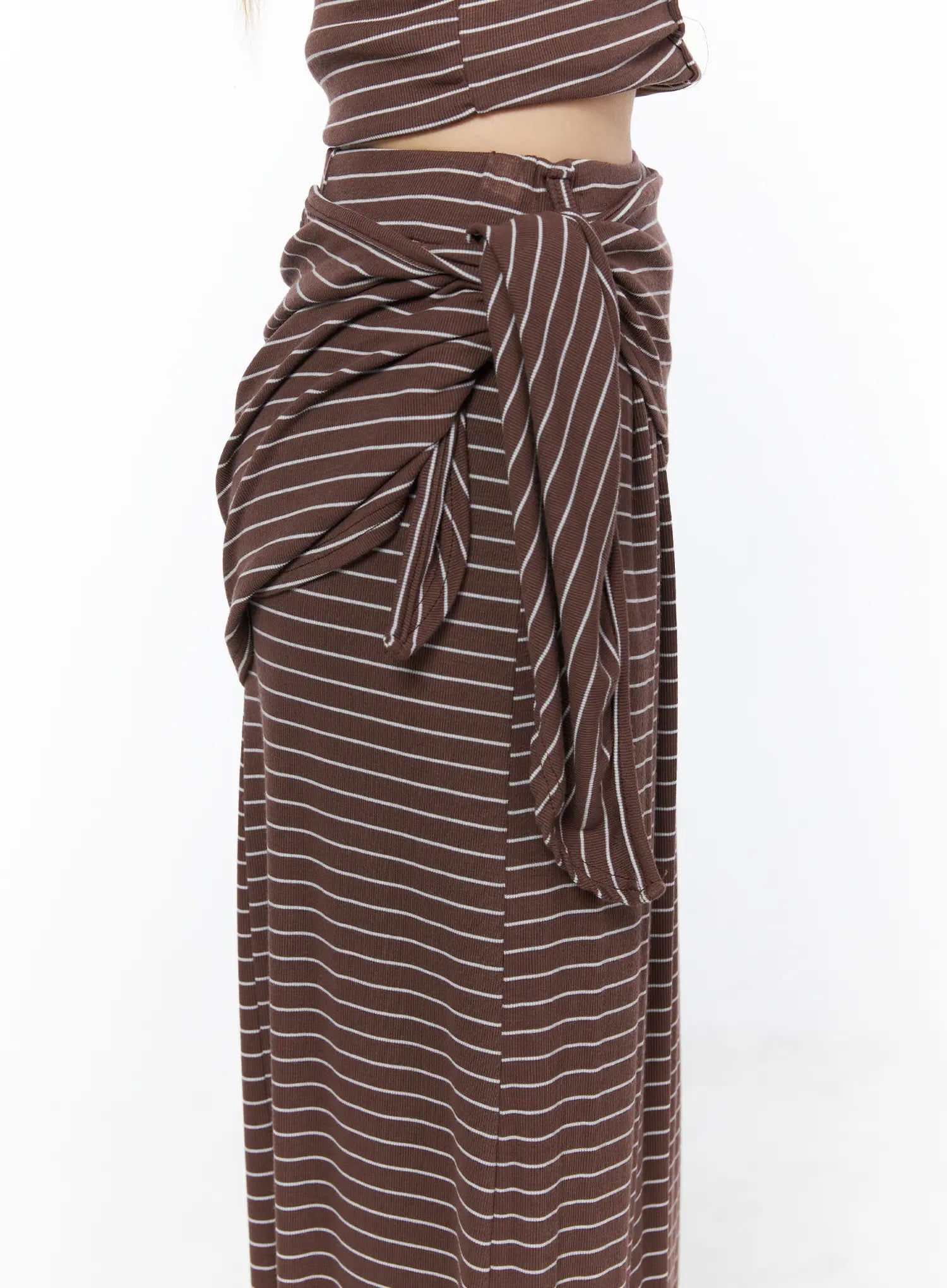 Striped Wrap Maxi Skirt CL502 Brown close-up side detail showing voluminous draped tie knot gathered fabric and ribbed stripe texture at hip on model