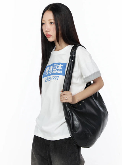 Studded Large Hobo Bag CL527 Black three-quarter front view on model in white graphic tee holding bag strap, slouchy faux leather hobo with silver dome studs