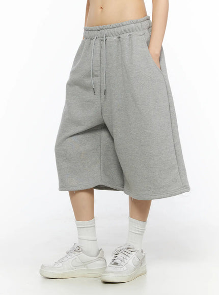 Studded Sweatshorts CU530 Gray side view on model showing wide-leg hemline and back patch pocket with silver ball-stud cross accent white knit hoodie styled over