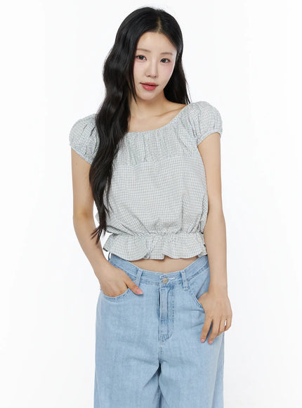 Summer Plaid Off-Shoulder Blouse IU525 Light blue upper-body front view on model with hand in pocket showing scoop neckline and cap puff sleeves with denim