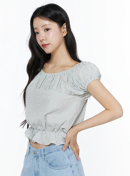 Summer Plaid Off-Shoulder Blouse IU525 Light blue side close-up on model with hand on hip showing ruffle hem, elastic waist detail, and gingham texture