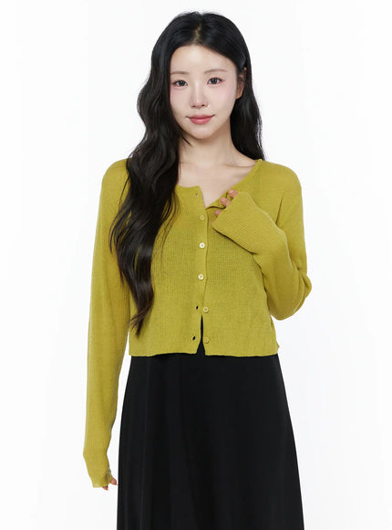 Summer Ribbed Crop Cardigan IU525 Yellow front shot on model with hand on chest showing ribbed knit crop cardigan with button front and long sleeves over black skirt