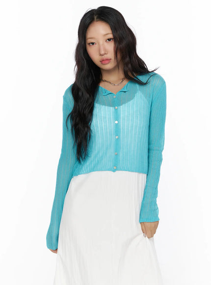 Summer Sheer Crop Cardigan CL510 Blue front shot on model showing sheer ribbed knit, collar neckline, silver buttons and long sleeves over white maxi dress