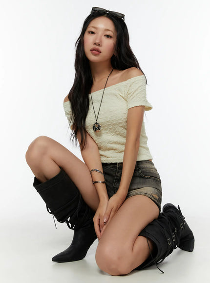 LEWKIN Textured Off-Shoulder Top CU529 Light yellow front view on seated model wearing black knee-high lace-up boots and denim mini skirt with pendant necklace