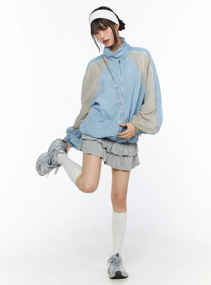 Tiered Flare Mini Skirt CU530 Gray full-body front shot on model styled with blue colorblock windbreaker, visor, and silver sneakers, leg raised