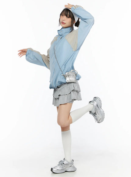 Tiered Flare Mini Skirt CU530 Gray full-body side shot on model styled with blue windbreaker and visor, one leg raised, silver mini crossbody bag