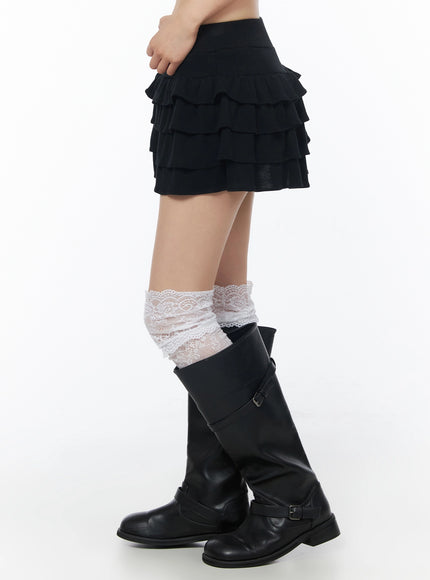 Tiered Ruffle Mini Skirt IU525 Black side waist-down view on model highlighting ruffle tiers and white lace socks over black buckle boots