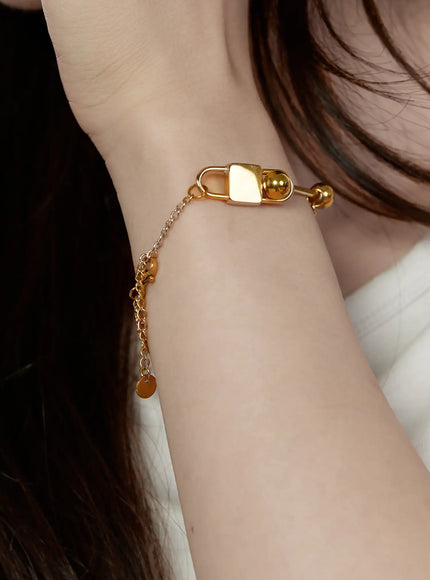 Titan Bar Bracelet IL522 Gold close-up on model's wrist showing padlock charm and bar detail with adjustable chain extender and coin drop