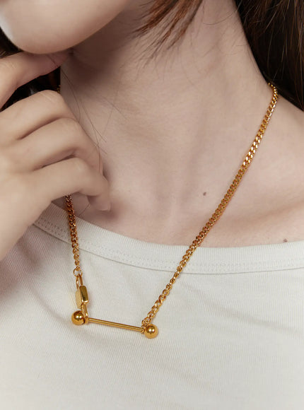 LEWKIN Titan Bar Necklace IL522 gold front close-up on model neck, bar pendant with ball ends on curb chain over white tee